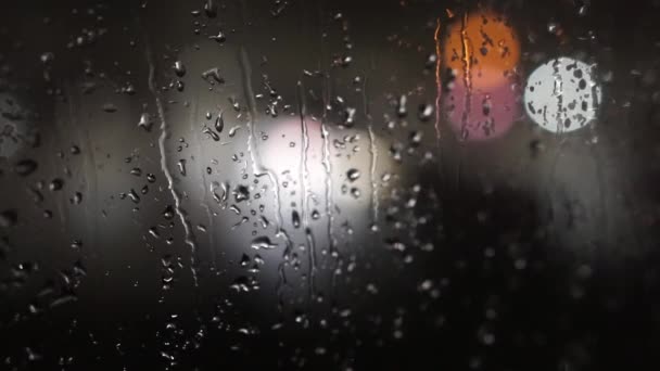 Közelről láthatjuk, ahogy a vízcseppek üvegre esnek éjszaka. Színes közlekedési bokeh lámpa. Zuhog az eső az ablakon. Esős évszak, ősz. Az esőcseppek lefolynak. — Stock videók