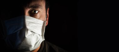 Alçak bir anahtarla tıbbi maske takan bir adamın portresi. Dünya çapında bir trajedi. COVID-19 virüs salgını uyarısı.