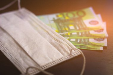 100 Euro 'luk banknotlarda tıbbi maske. Seçici odaklanma. Coronavirus COVID-19 salgınında tıbbi ekipman ve maskeler için yüksek fiyatlar kavramı.