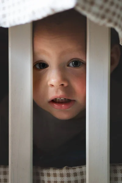 Крупным планом портрет улыбающегося очаровательного маленького белого мальчика, играющего за забором для кроваток — стоковое фото