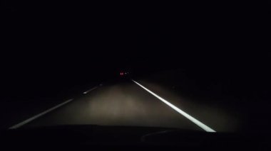 Gece taksisinden bir görüntü. Farlar arabanın önündeki asfaltı aydınlatıyorlar. Yaklaşan araçların farları bazen görünür. Karanlıkta güvenli sürüş kavramı.