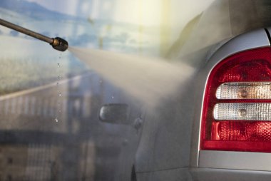 Bir adam suyun basıncıyla araba yıkar ve bardağı ovuşturur. Araba bakımı konsepti