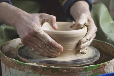 Çömlekçinin elleri çömlekçinin tekerine yakın çekim. Eski geleneksel sanat, el yapımı, kil ve seramik üretim. Yumuşak ışıkta çömlek atölyesi