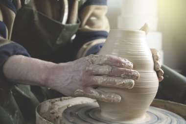Çömlekçinin elleri çömlekçinin tekerine yakın çekim. Eski geleneksel sanat, el yapımı, kil ve seramik üretim. Yumuşak ışıkta çömlek atölyesi