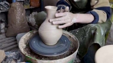 Çömlekçinin elleri çömlekçinin tekerine yakın çekim. Eski geleneksel sanat, el yapımı, kil ve seramik üretim. Yumuşak ışıkta çömlek atölyesi