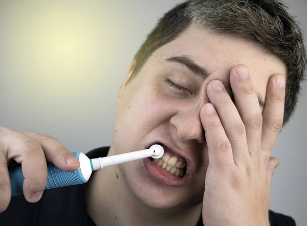 Sleepy man brushes his teeth with an electric brush. Oral hygiene concept. Tired man caring for teeth