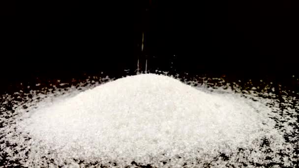 砂糖の小さな部分は 砂糖の山に注がれます 甘い歯の概念 黒の背景に砂糖のマクロビデオ顆粒 — ストック動画