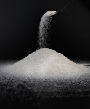 Siyah arka planda şekerli kaşık. Tatlıya bağımlılık kavramı. Granüle şekerin makro fotoğrafı.