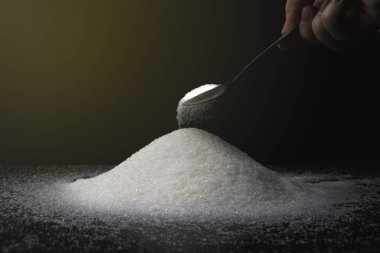 Siyah arka planda şekerli kaşık. Tatlıya bağımlılık kavramı. Granüle şekerin makro fotoğrafı.