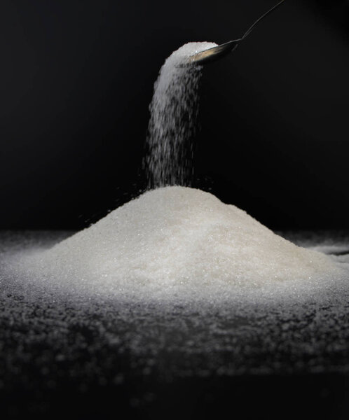 Spoon in sugar on a black background. The concept of addiction to sweets. Macro photo of granulated sugar.