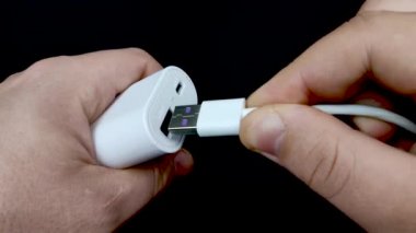 İçinde beyaz bir USB kablosu olan bir USB konnektörünün makro videosu. Güç bankasının dönüşünde, cihazın şarj edildiğini gösteren mavi ışıklar yanıyor..