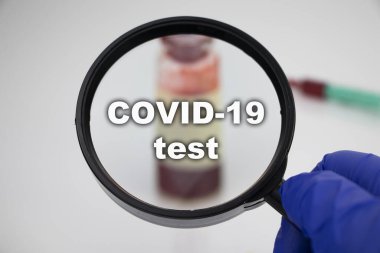 Diyabetik ketoasidoz (eton testi) için bir kan örneği. Doktorun elinde laboratuvar araştırmaları için üzerinde kan örneği olan bir test tüpünün bulunduğu bir büyüteç var..
