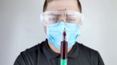 Erkek bir doktor kanla dolu bir şırıngaya bakar. Laboratuvarda analiz için kan örneği alıyorum. Metin için hafif arkaplan ve yer.