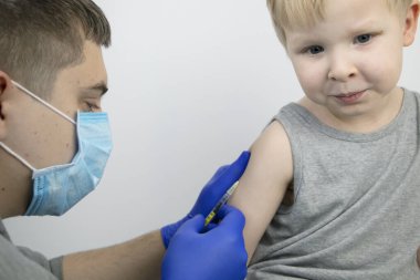 Bir doktor çocuğun omzuna aşı enjekte eder. Çocukların aşılanması ve bulaşıcı hastalıkların önlenmesi kavramı.