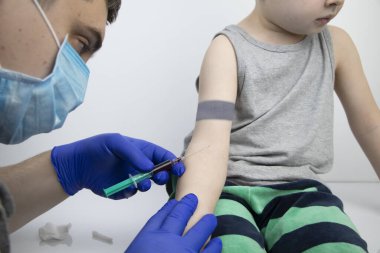 Doktor, çocuğun kanını damardan alır. Araştırma ve laboratuvar analizi için bir çocuktan kan almak