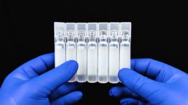İlaçlı veya aşılı plastik ampuller. Mavi eldivenli doktor ilacı inceliyor. Makro video. Modern tıp konsepti