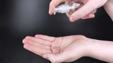 Siyah arka planda antiseptikle kadın elleri işleniyor. Antibakteriyel jel ve dezenfektan. Vücudu mikroplardan koruma kavramı. Ellerine jöle döküp cildine sürterek..