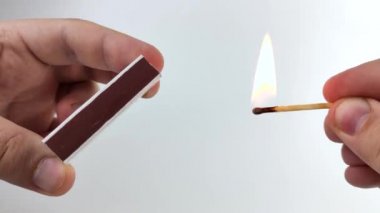 Erkeklerin elleri kutularda kibrit yakıyor. Kibrit kafa ateşlemesinin makro videosu. Kibritlerin güvenli kullanımının bir işareti olarak beyaz arkaplanda ateş yakma kavramı.