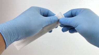 Mavi eldivenli bir doktor tek kullanımlık steril tıbbi spatulayı açar. Ağız boşluğunu ve bademcikleri incelemek için kullanılan tahta bir spatula makro videosu..