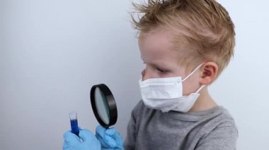 Çocuk bir doktor ve bilim adamını oynuyor. Tıbbi maskeli bir çocuk, büyüteçle test tüpünde ilaç üzerinde çalışıyor. Tıp mesleklerinin tanıtımı ve eğitimi
