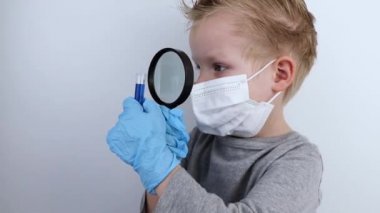 Çocuk bir doktor ve bilim adamını oynuyor. Tıbbi maskeli bir çocuk, büyüteçle test tüpünde ilaç üzerinde çalışıyor. Tıp mesleklerinin tanıtımı ve eğitimi
