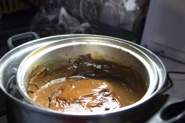 Su banyosunun altındaki bir tavada erimiş çikolata. Kendi mutfağında sıcak çikolata yapmak.