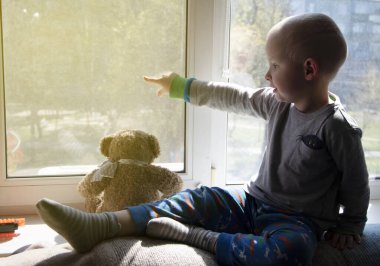 Pandemik izolasyon - koronovirüs salgını, covid-19. Çocuk karantina sırasında pencerenin kenarında otururken ne yazık ki pencereden dışarı bakıyor. Karantina altındaki çocuklar, evde eğitim, evde kalmak.