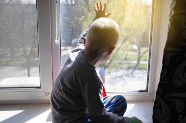 Pandemik izolasyon - koronovirüs salgını, covid-19. Çocuk karantina sırasında pencerenin kenarında otururken ne yazık ki pencereden dışarı bakıyor. Karantina altındaki çocuklar, evde eğitim, evde kalmak.