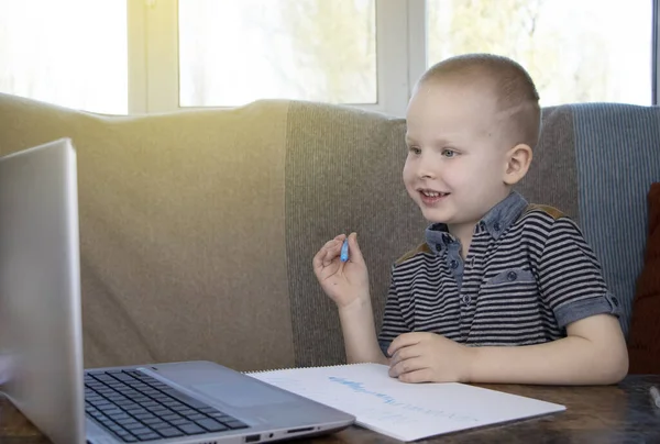 Preschooler is engaged in home schooling. The boy sits at a table, writes, draws and learns online on the Internet. Quarantine due to the coronovirus pandemic, covid-19