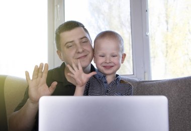 Baba ve oğul, akrabaları ya da öğretmenleriyle video bağlantısıyla konuşuyorlar. İnternet üzerinden çevrimiçi iletişim konsepti ve dizüstü bilgisayarda bir kamera. Karantina ve tecrit sırasında büyükanne ve büyükbabayı aramak.