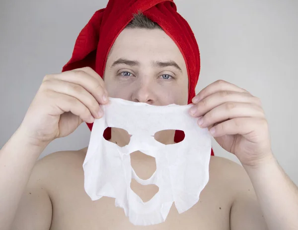 Vtipný Muž Červeným Ručníkem Nasazuje Hydratační Látkovou Masku Obličej Koncept — Stock fotografie