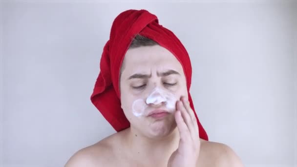 頭に赤いタオルを被った面白い男が顔の世話をし 洗濯に泡を使用します 男性のセルフケア スパトリートメント 男性化粧品のコンセプト — ストック動画