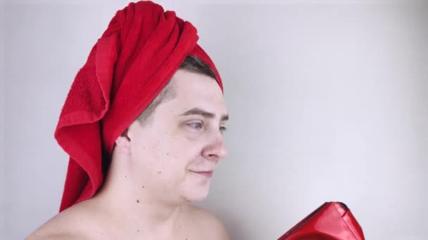 一个头戴红色毛巾的有趣的男人嗅了闻 尝了尝 脸上沾满了奶油 男性自我护理 温泉治疗和男性化妆品的概念 — 图库视频影像