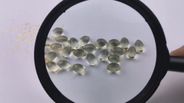Bir insan büyüteç altında D3 vitamini kapsüllerini inceler. Kapsüllerin üzerinden geçen bir büyüteç onları büyük yapıyor. Sağlık Hizmetleri Konsepti