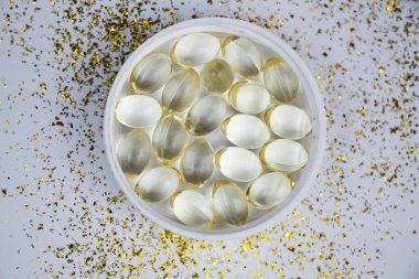 Vitamin D3 gelatin capsules on a white background. The fat-soluble solar vitamin cholecalciferol glows yellow and glistens. Place for text clipart