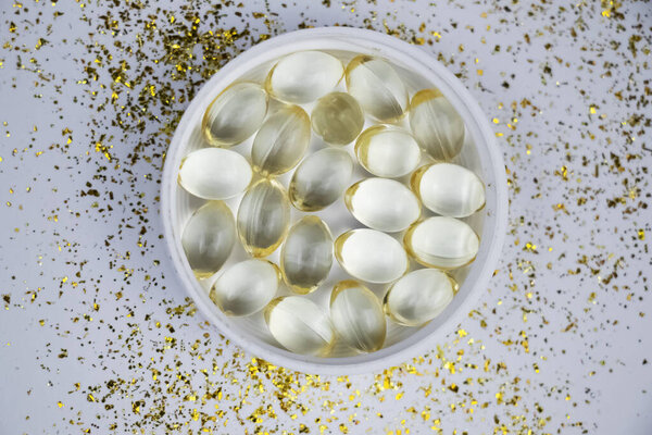 Vitamin D3 gelatin capsules on a white background. The fat-soluble solar vitamin cholecalciferol glows yellow and glistens. Place for text