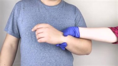 Erkek bileği acıtır. Travmatolog bir eli muayene ediyor. Bilek ağrısı tünel sendromu, burkulma, tendon dejenerasyonu, eklem iltihabı belirtisi.