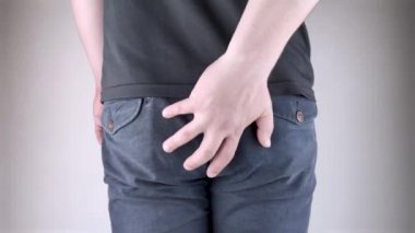 A man holds his hands to the ass feeling pain. Conversion of pain in the rectum, hemorrhoids and pain in the excretory system of the body. Frequent bowel movements.