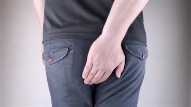 A man holds his hands to the ass feeling pain. Conversion of pain in the rectum, hemorrhoids and pain in the excretory system of the body. Frequent bowel movements.