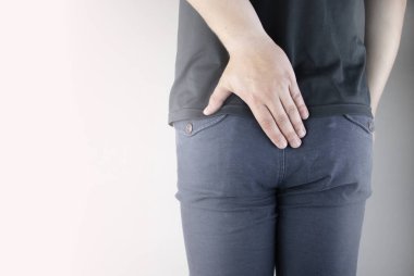 A man holds his hands to the ass feeling pain. Conversion of pain in the rectum, hemorrhoids and pain in the excretory system of the body. Frequent bowel movements.