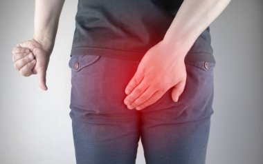 A man holds his hands to the ass feeling pain. Conversion of pain in the rectum, hemorrhoids and pain in the excretory system of the body. Frequent bowel movements.