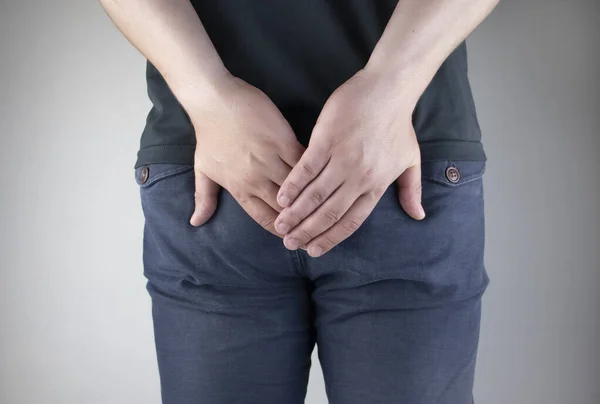 A man holds his hands to the ass feeling pain. Conversion of pain in the rectum, hemorrhoids and pain in the excretory system of the body. Frequent bowel movements.