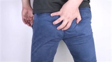 A man holds his hands to the ass feeling pain. Conversion of pain in the rectum, hemorrhoids and pain in the excretory system of the body. Frequent bowel movements.