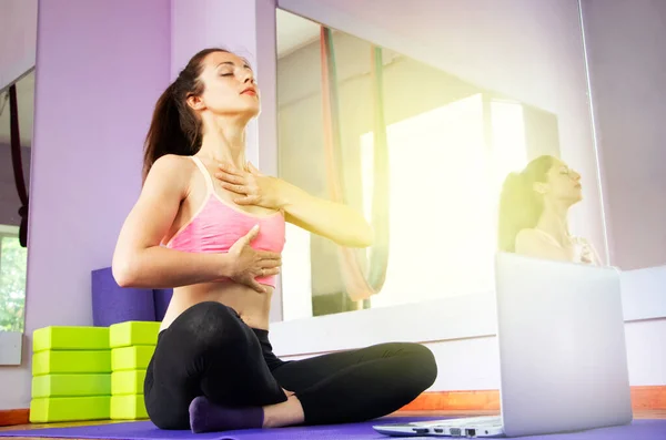 Fitness and yoga trainer teaches via laptop. Wireless technology in sports, self-isolation . The girl shows exercises in the gym on the mat. The concept of distance learning.