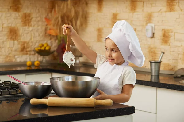 キッチンの女の子シェフの帽子をかぶって生地でスプーンを持っていて — ストック写真