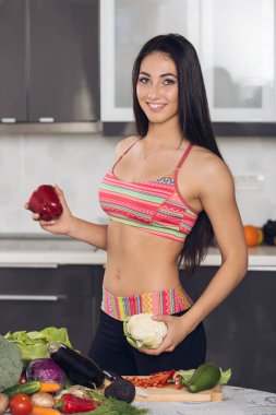 Mutfakta elinde kırmızı biber ve karnabahar tutan mutlu, zinde bir kadın.