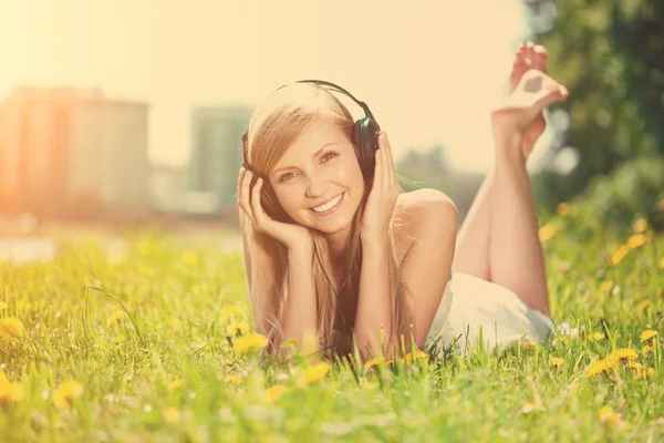 笑みを浮かべて女性美人屋外のヘッドフォンで音楽を聴く — ストック写真