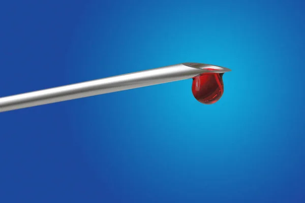Macro view of drop of blood from needle syringe on blue backgrou — Stock Photo, Image