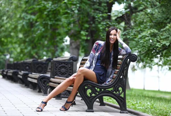Portrait of the brunette with long hair sitting on a park bench — Stock Photo, Image