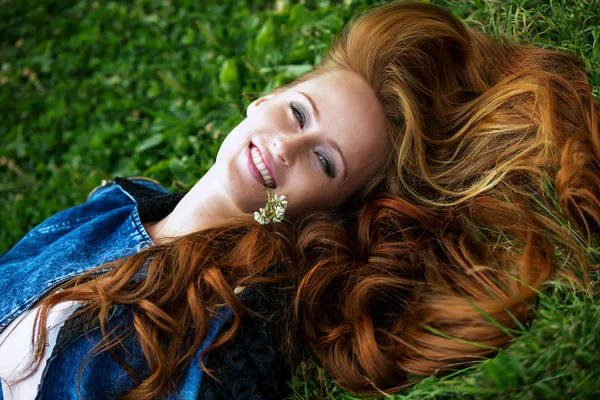 Rödhårig flicka liggande på gräset och ler — Stockfoto